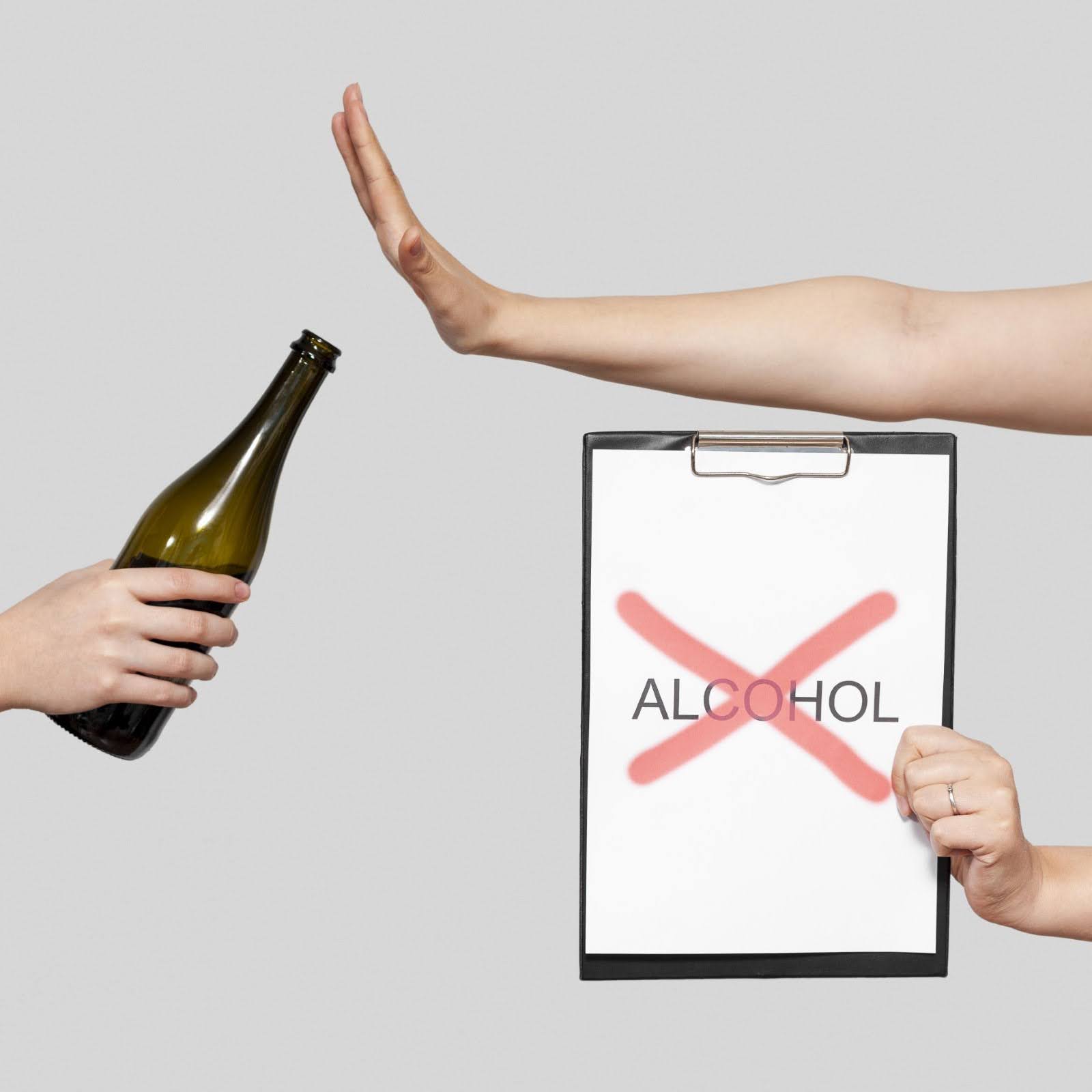Side view of a hand holding a bottle of wine and another pair of hands saying no to it by holding a page attached to a clipboard showing the word 'alcohol' struck out.