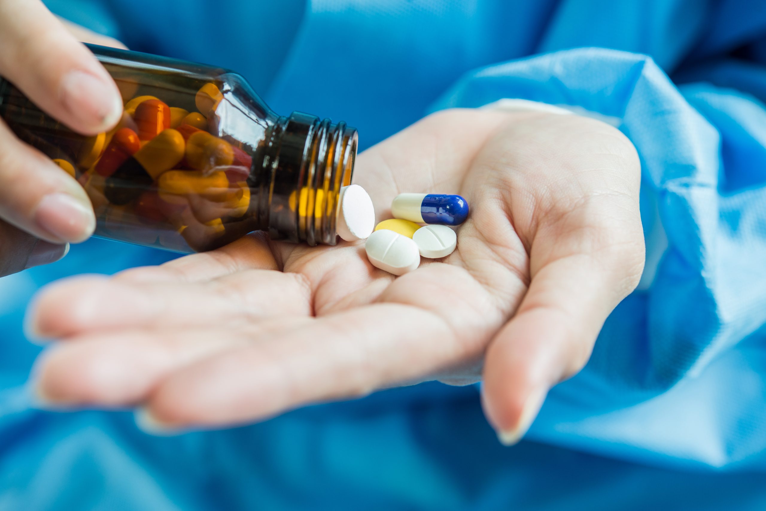 A person's hand pours medicine pills out of a bottle